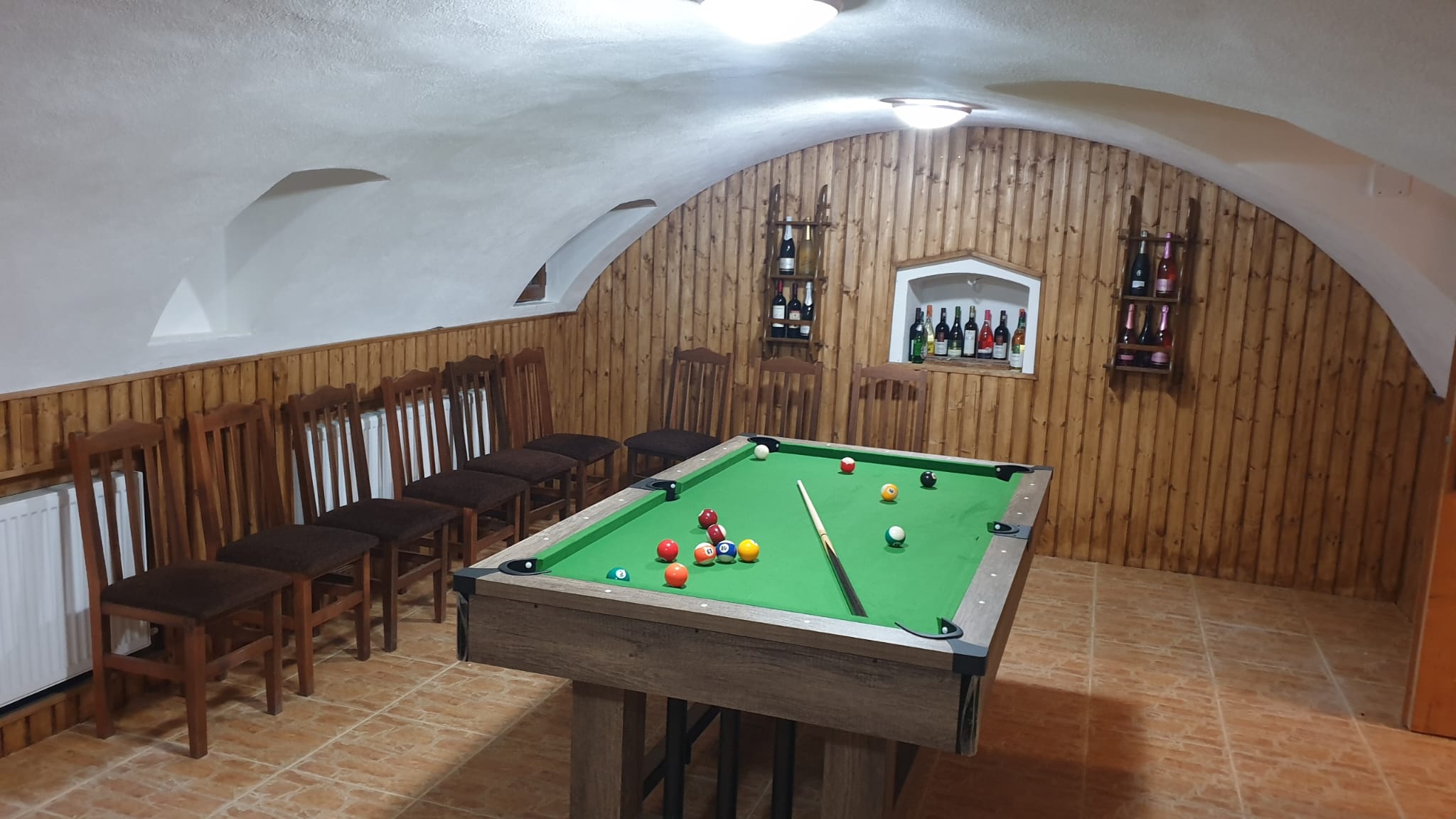 Masă de biliard sub boltă de cărămidă, cu bar de vinuri în fundal