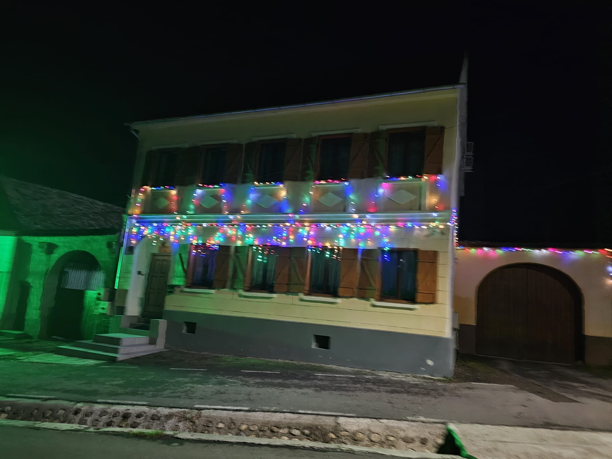 Fațada Casei La Saal noaptea, luminată cu ghirlande colorate, obloane de lemn