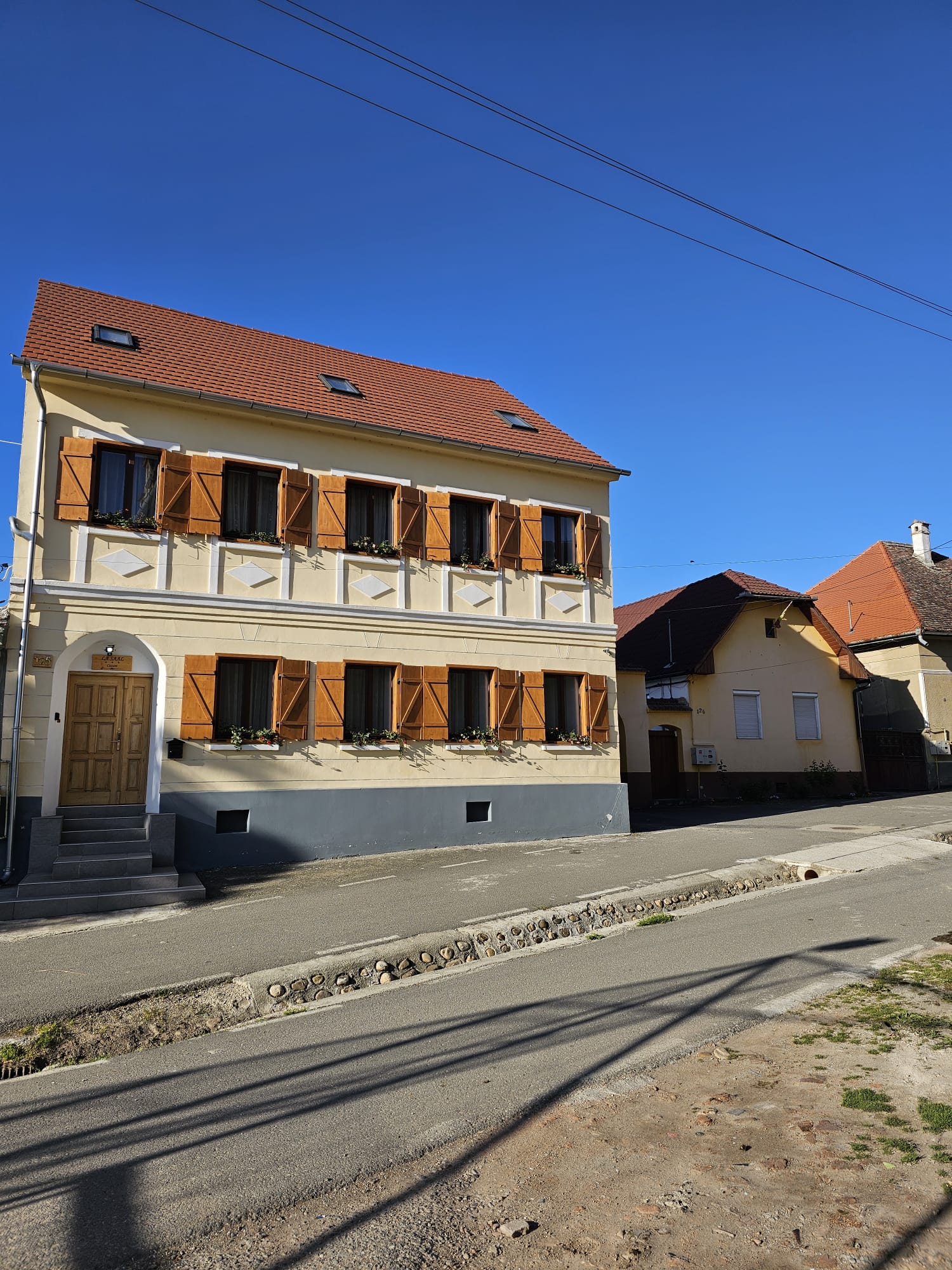 Fațada casei, ziua, cu obloane maro și firma Cazare deasupra ușii