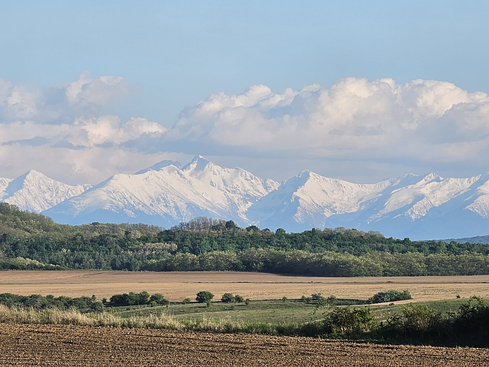 Panoramă cu munți sub cer înnorat, câmp arat