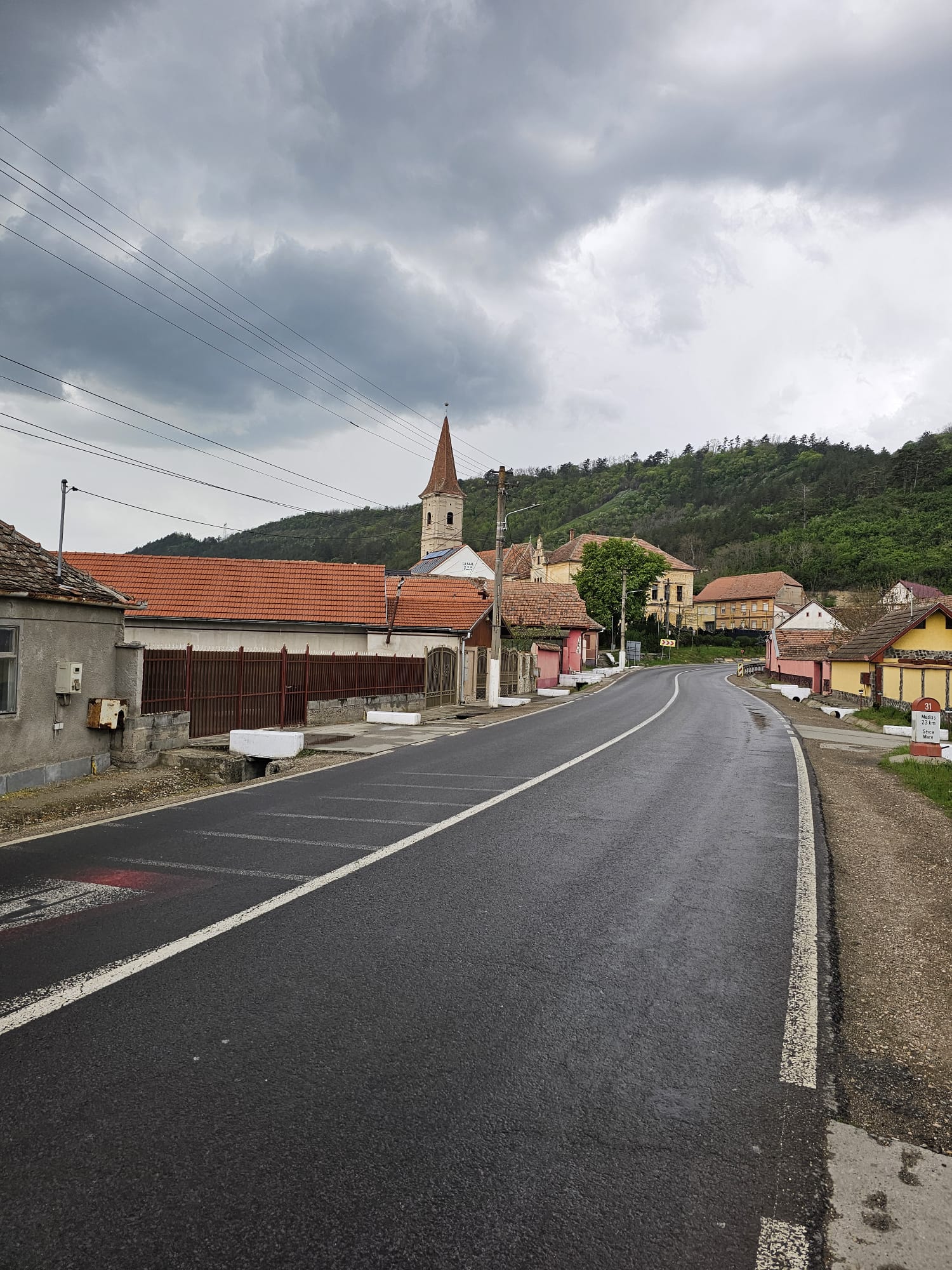 Stradă din sat sub cer înnorat, turn de biserică săsească