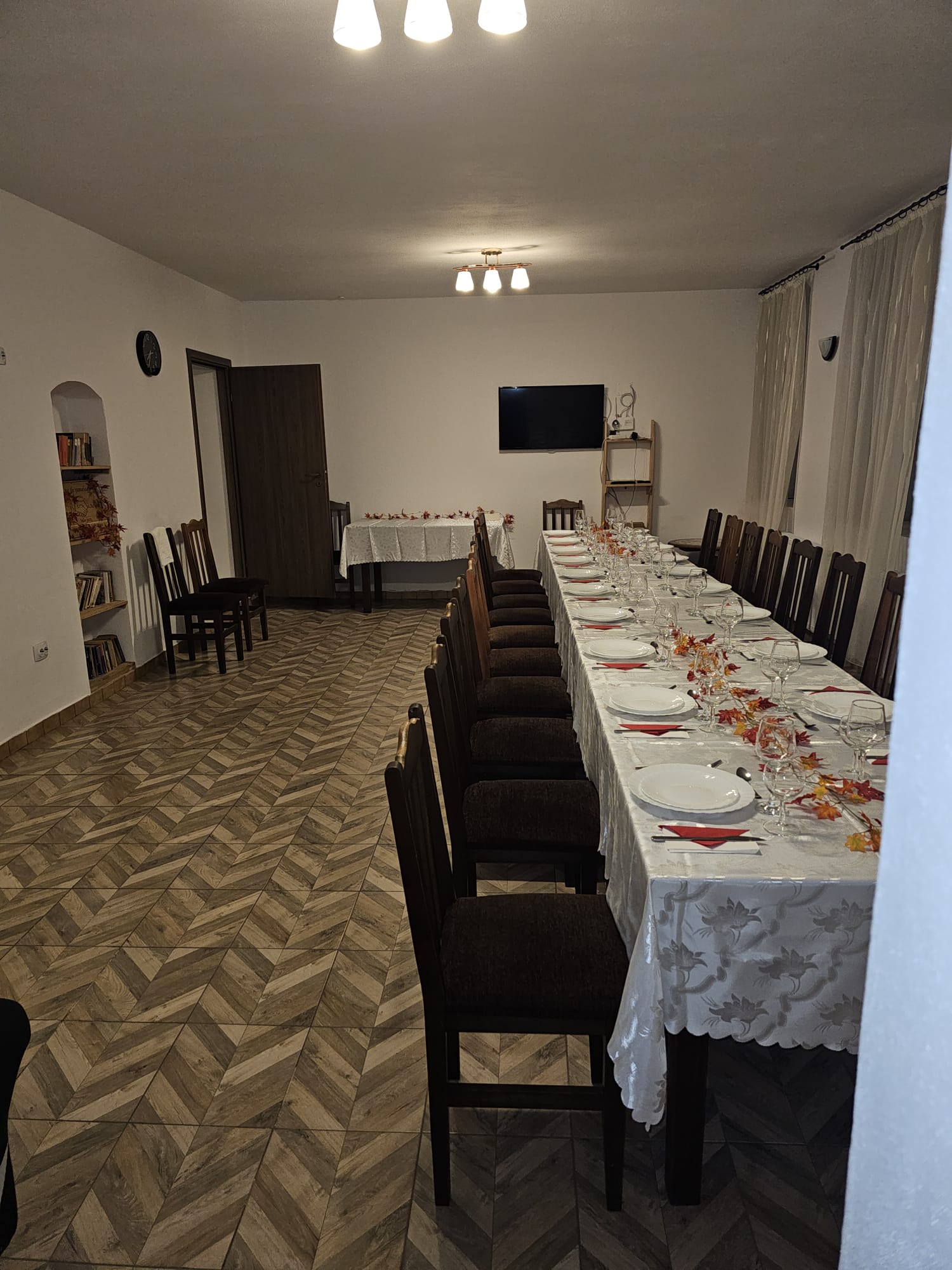 Salonul mare, cu masă festivă lungă, raft cu cărți în firidă și TV montat pe perete